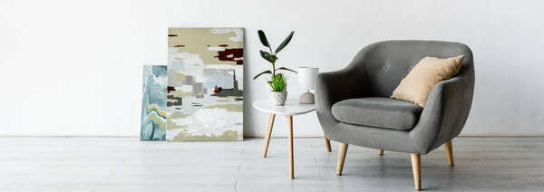 panoramic crop of comfortable armchair near coffee table with green plants, lamp and paintings in living room 