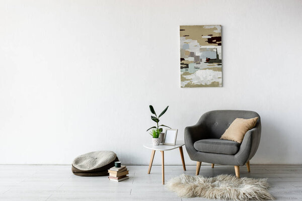 comfortable armchair near coffee table with green plants, frame and painting on wall in modern living room 