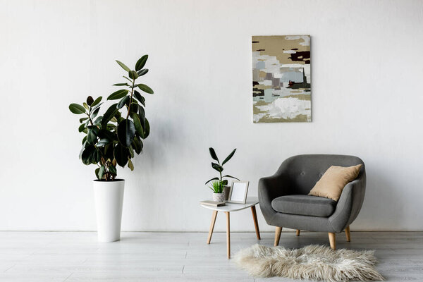 grey armchair near coffee table with green plants and frame in modern living room 