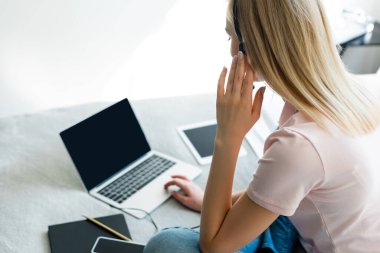 Laptop ve dijital tablet yakınındaki kulaklığa dokunan serbest çalışanın seçici odak noktası.