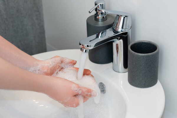 cropped view of girl washing soapy hands in bathroom 