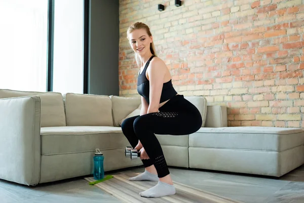 Deportista Feliz Haciendo Ejercicio Cuclillas Con Mancuernas Cerca Botella Deportes — Foto de Stock