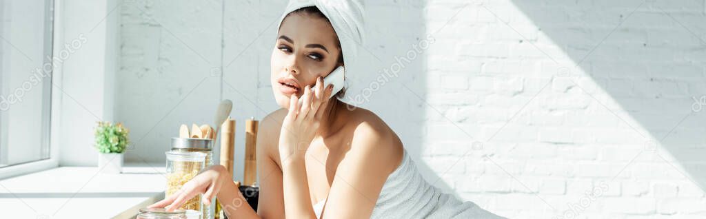 Panoramic shot of sensual woman in towels talking on smartphone in kitchen 