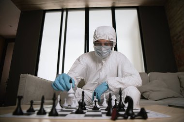 Kişisel koruyucu ekipman ve tıbbi maske takmış satranç oynayan bir adamın seçici odağı 