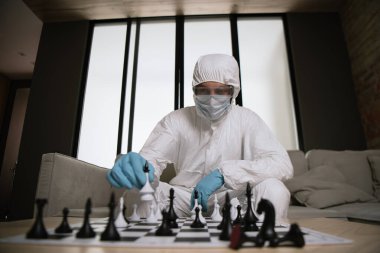 selective focus of man in personal protective equipment and medical mask playing chess  clipart