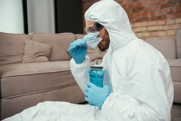 Homem Barbudo Terno Hazmat Tocando Máscara Médica Segurando Garrafa Esportes — Fotografia de Stock