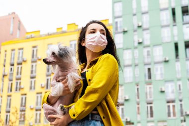 Pembe tıbbi maskeli çekici bir kız şehirde köpekle yürüyor.
