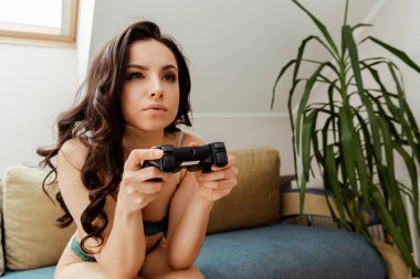 KYIV, UKRAINE - 16 Nisan 2020: kendini tecrit sırasında koltukta joystick ile iç çamaşırı oyunu oynayan konsantre kadın