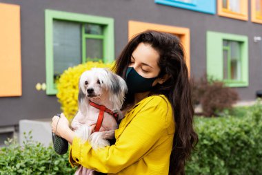 Siyah tıbbi maskeli güzel bir kadın şehirde köpekle yürüyor.