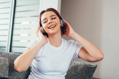 Karantina sırasında koltukta oturmuş kulaklıkla müzik dinleyen pozitif kız.