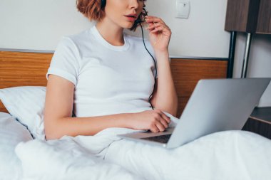 Kulaklık ve laptopla izolasyon sırasında yatakta video görüşmesi yapan kız görüntüsü.