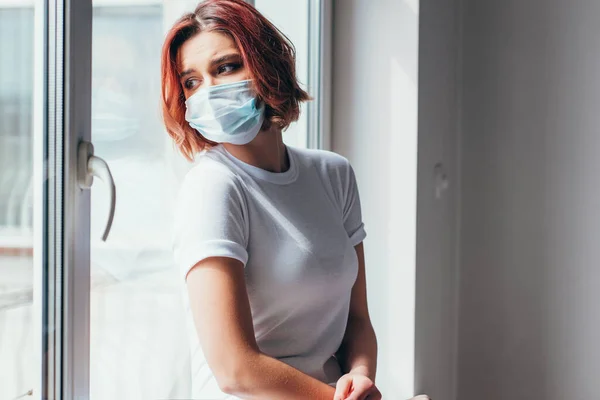 Hermosa Chica Triste Máscara Médica Mirando Través Ventana Durante Cuarentena —  Fotos de Stock