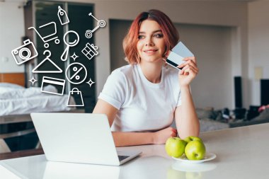 Bilgisayarlı, kredi kartlı ve mutfaktaki elmalı alışveriş tabelalarıyla internetten alışveriş yapan pozitif bir kız. 