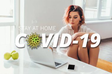 Kulaklıklı güzel bir kadın evde COVID-19 harfleriyle karantina sırasında mutfakta elma ve akıllı telefon kullanıyor. 