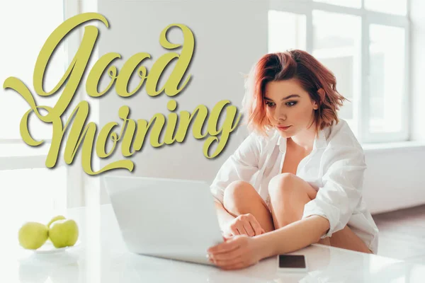 stock image attractive girl with headphones using laptop on kitchen with apples and smartphone during self isolation with good morning lettering 