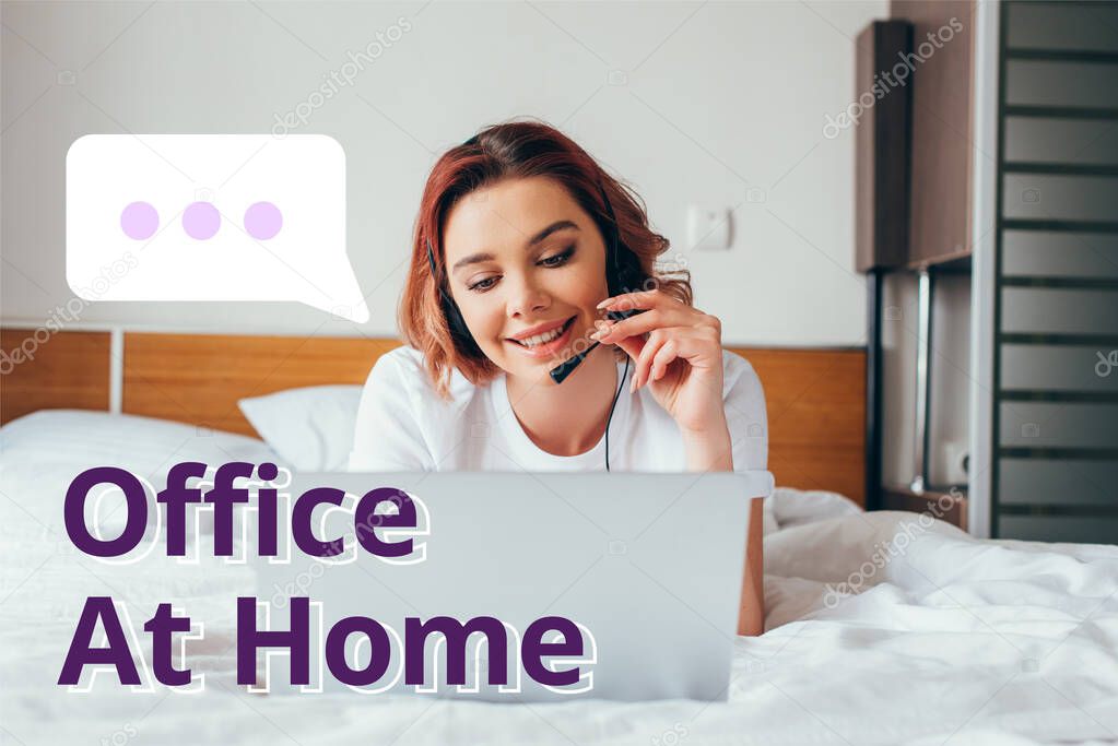 beautiful happy freelancer making video call with headset and laptop in bed during self isolation with office at home lettering 