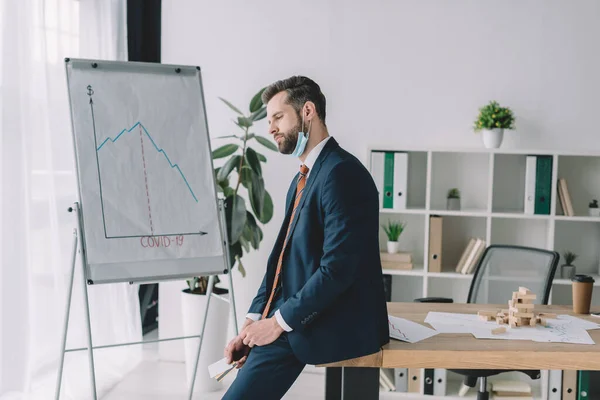 Upset businessman holding credit cards while standing near flipchart with graphs showing recession — Stock Photo