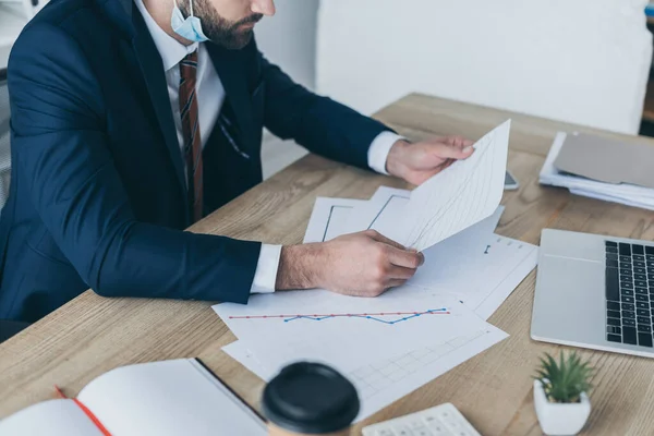 Vista recortada del hombre de negocios mirando papeles con gráficos y gráficos mientras está sentado en el lugar de trabajo - foto de stock