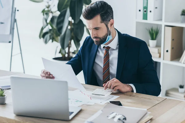 Seriöser, durchdachter Geschäftsmann, der am Arbeitsplatz in der Nähe des Laptops mit Dokumenten arbeitet — Stockfoto