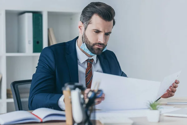 Enfoque selectivo od serio, empresario reflexivo mirando documentos mientras está sentado en el lugar de trabajo - foto de stock