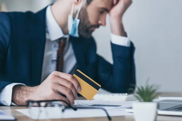 Selektiver Fokus eines verärgerten Geschäftsmannes mit Kreditkarte am Arbeitsplatz sitzend mit geschlossenen Augen und gesenktem Kopf — Stockfoto