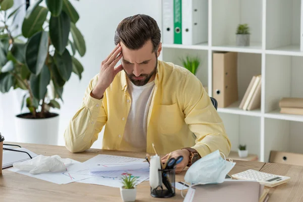 Pensativo empresario tocando la cabeza mientras está sentado en el lugar de trabajo y mirando los documentos - foto de stock