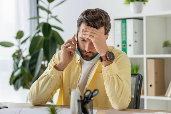 Selective focus of depressed businessman touching forehead while talking on smartphone in office — Stock Photo