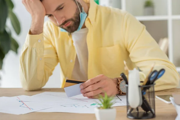 Selective focus of depressed businessman holding hand near head while looking at credit card — Stock Photo
