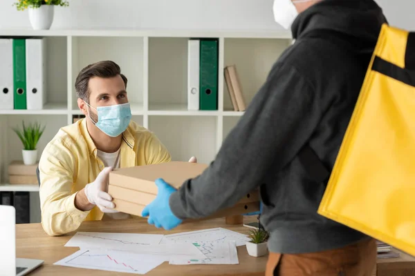 Vista parziale di consegna cibo uomo dando scatole di pizza per l'uomo d'affari in maschera medica e guanti di lattice — Foto stock