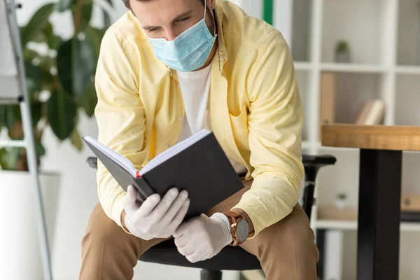 Homme d'affaires en masque médical et gants en latex à la recherche d'un ordinateur portable dans le bureau — Photo de stock