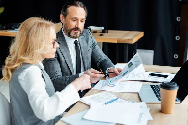 Selektiver Fokus von Geschäftsleuten, die mit Papieren in der Nähe digitaler Geräte und Pappbecher auf dem Tisch arbeiten — Stockfoto