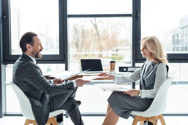 Side view of smiling businessman giving document to businesswoman near laptop on table — Stock Photo