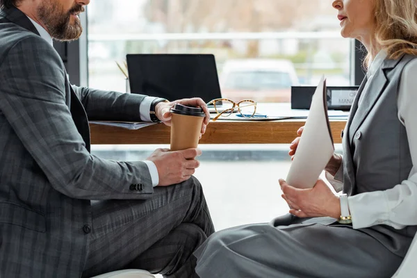 Cropped view of business people with coffee to go and paper folder sitting at table in office — Stock Photo