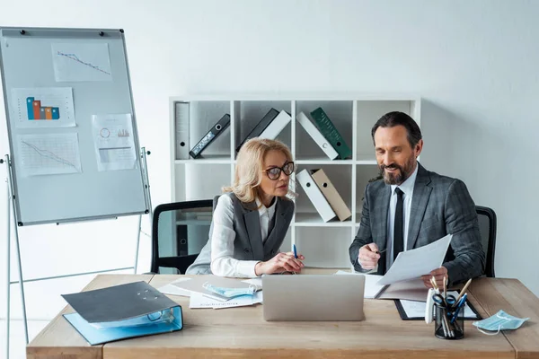 Sonriente hombre de negocios sosteniendo documento cerca de la mujer de negocios en la mesa en el cargo — Stock Photo