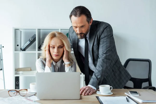 Орієнтована бізнес-леді дивиться на ноутбук поруч з бізнесменом під час роботи в офісі — стокове фото