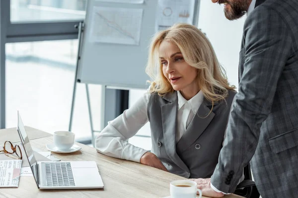 Geschäftsleute arbeiten mit Laptop neben Kaffeetassen und Zeitung auf dem Tisch — Stockfoto