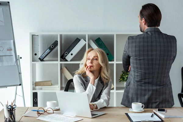 Nachdenkliche Geschäftsfrau schaut in der Nähe von Laptop und Geschäftsmann im Büro weg — Stockfoto