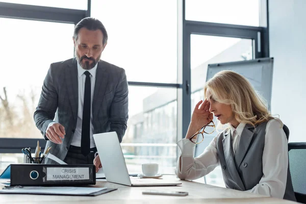 Selektiver Fokus der Geschäftsfrau auf Laptop in der Nähe von Geschäftsleuten und Ordner mit Krisenmanagement im Büro — Stockfoto