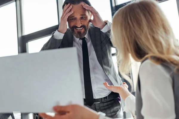 Selektiver Fokus eines lächelnden Geschäftsmannes in der Nähe einer Geschäftsfrau, die Papier im Büro hält — Stockfoto