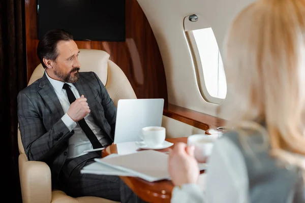 Selective focus of businessman with laptop sitting near businesswoman with cup of coffee in plane — Stock Photo