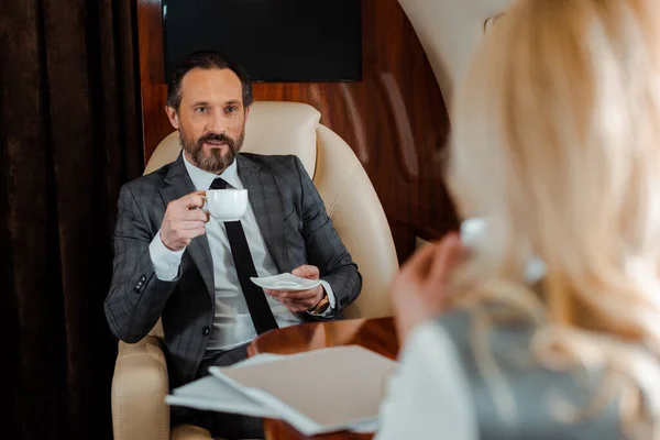 Enfoque selectivo del hombre de negocios con taza de café mirando a la mujer de negocios en el avión - foto de stock