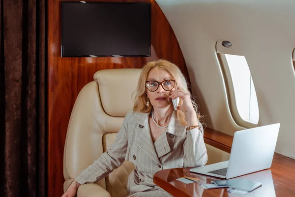 Geschäftsfrau spricht im Flugzeug mit Smartphone neben Kreditkarte und Laptop auf Tisch — Stockfoto