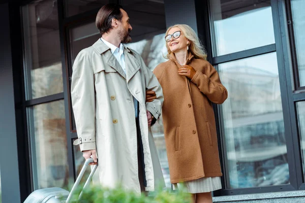 Focus selettivo della donna d'affari sorridente che guarda l'uomo d'affari con la valigia sulla strada urbana — Foto stock