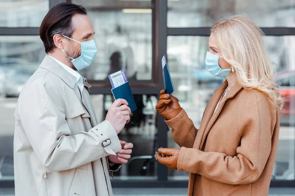 Side view of business couple looking at each other while holding passports with air tickets near building — Stock Photo