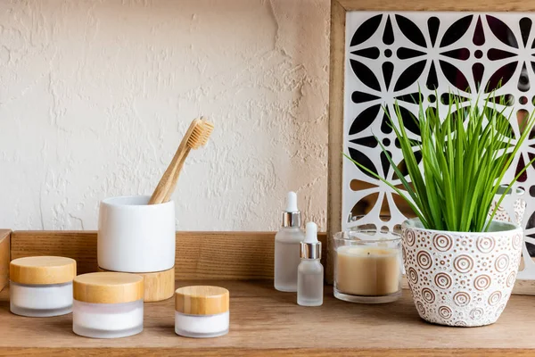 Prateleira de madeira com escovas de dentes, recipientes e garrafas perto de vela e planta verde — Fotografia de Stock