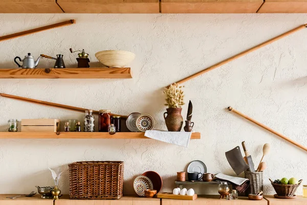 Clay mugs and bowls on shelves near knifes raw eggs and tasty fruits in kitchen — Stock Photo