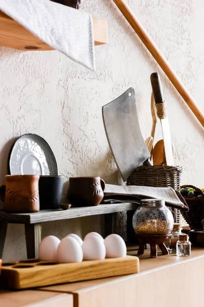 Selective focus of clay mugs near sharp knifes, cotton napkins and raw eggs — Stock Photo