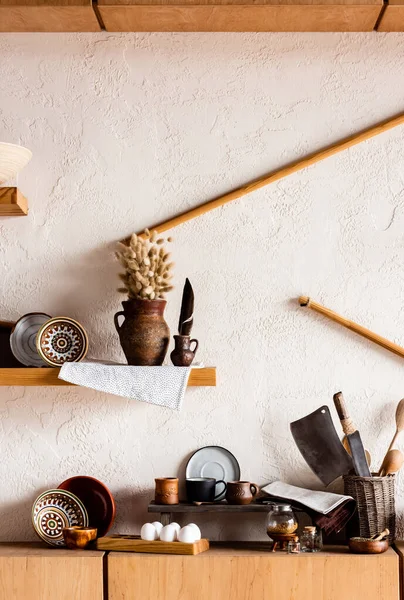 Catkins in clay jug near bowls, cups, knifes, and raw eggs in kitchen — Stock Photo