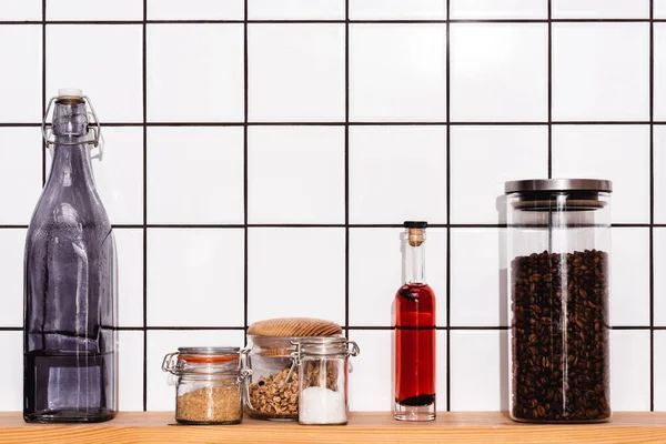 Frascos con granola, arroz, sal marina y café cerca de botellas en el estante - foto de stock