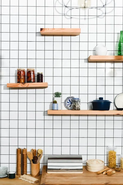 Canned tomatoes in jars near plants, jars, bamboo steamer and cooking utensils on shelves — Stock Photo